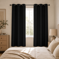 Two solid black grommet curtain panels in a warm neutral bedroom